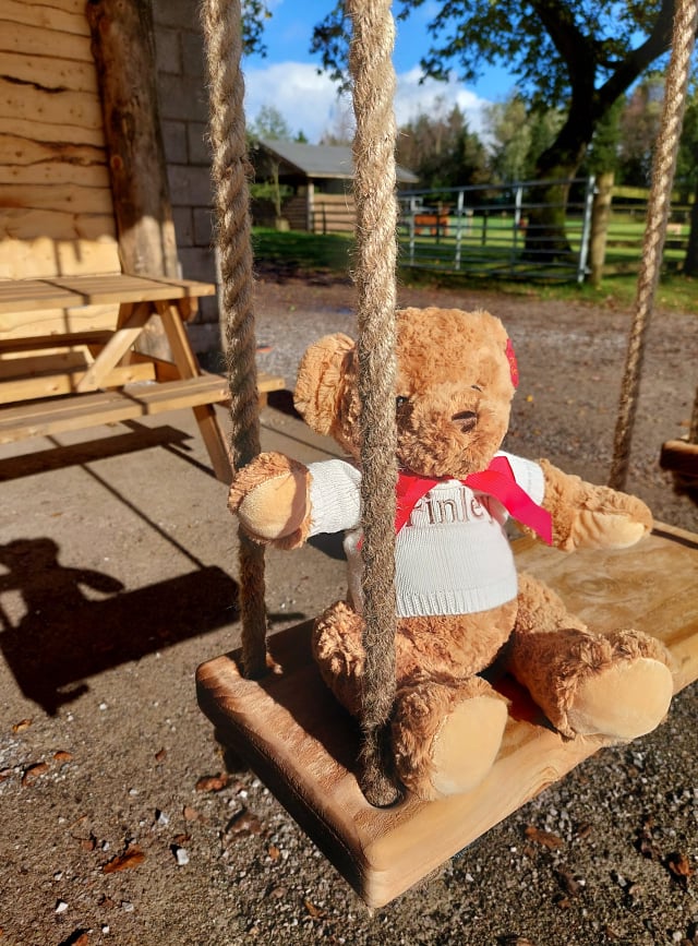 personalised teddy bear on wooden swing with red bow